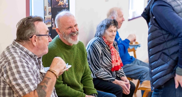 A middle age man talking to someone in a group setting, smiling and laughing.